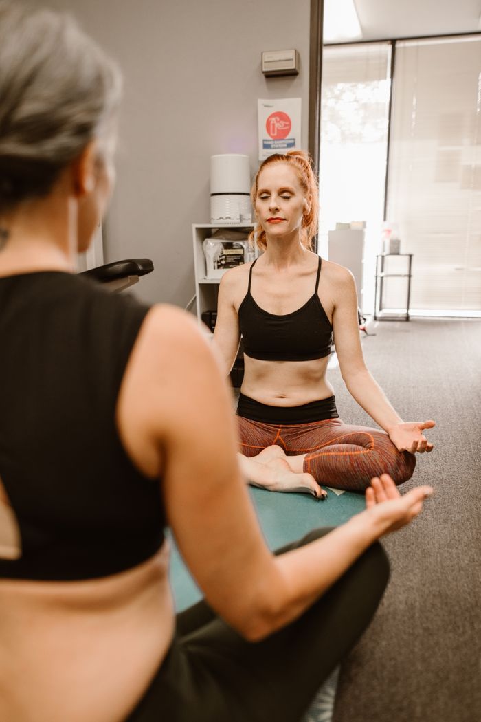 About Two women meditating indoors, focusing on mindfulness and wellness.