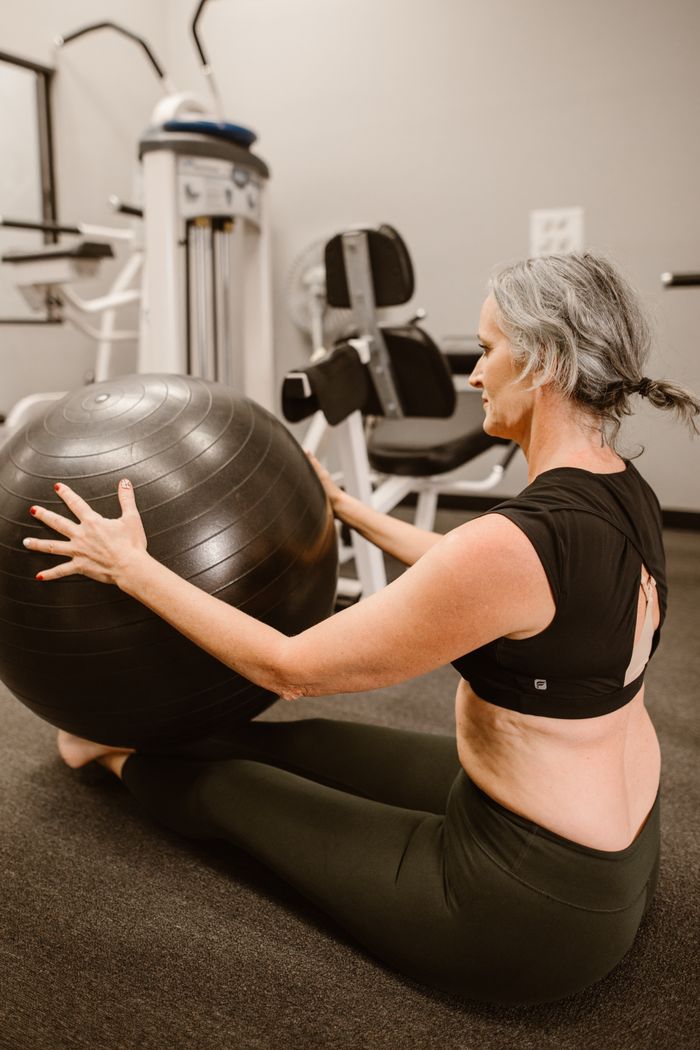 gallery-02 A midlife woman in activewear using a stability ball for fitness in an indoor gym.